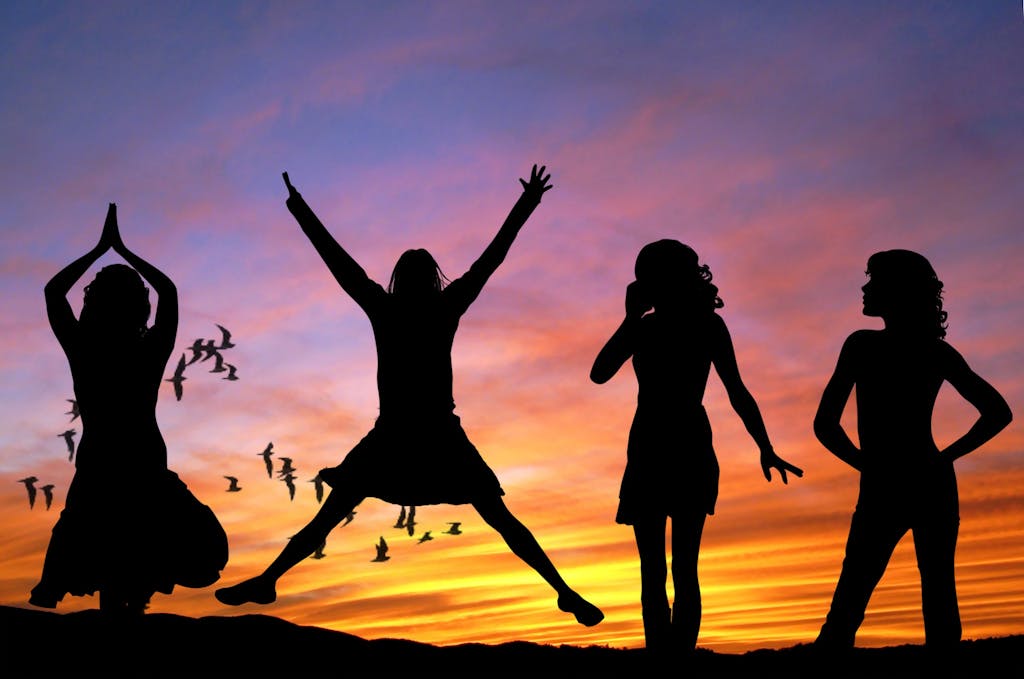 Navigating the A-Z of Menopause: Your Guide to Understanding and Thriving 8 Silhouetted group of women joyfully jumping and posing against a vibrant sunset sky with birds flying.